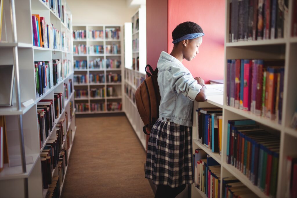 Attentive schoolgirl reading book in library