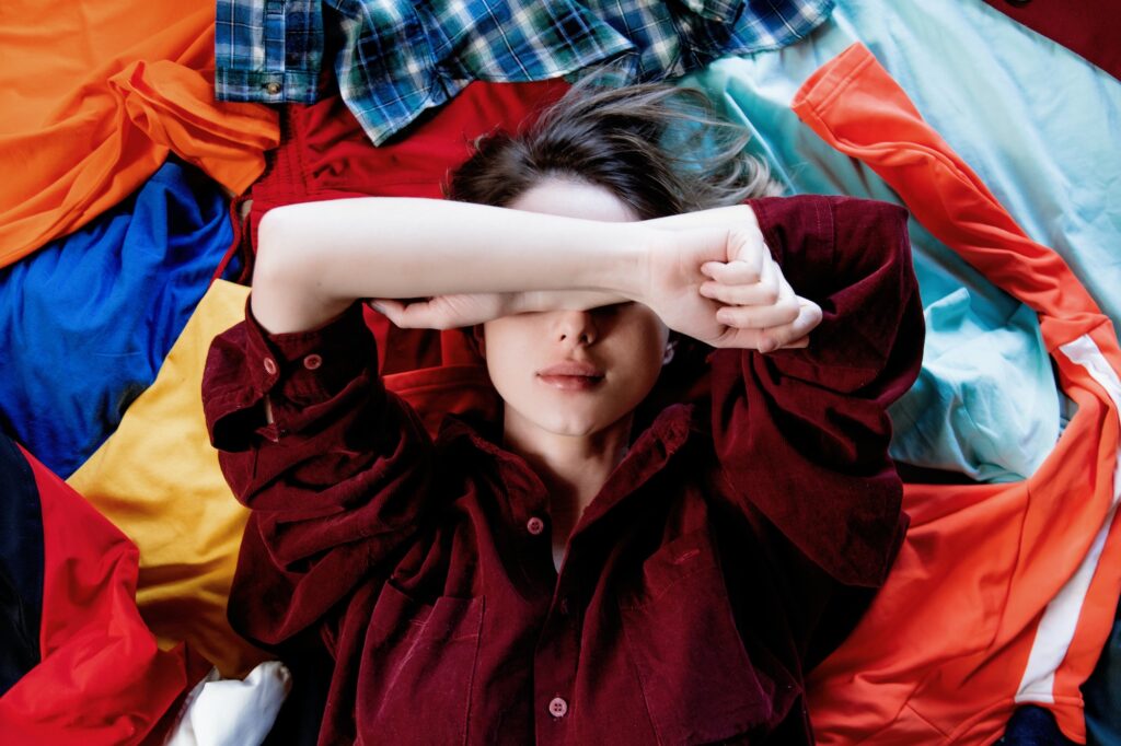 Upset woman keep hands over head and lying on clothes.